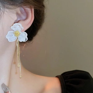 Detail of white acrylic flower earrings with gold tassel fringe on model