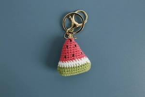 Macro detail of hand-knitted watermelon keychain showing cotton yarn texture and gold ring