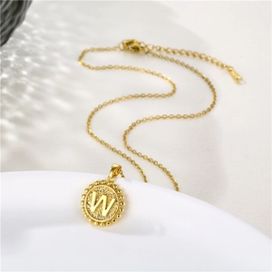 Close-up of golden round initial W necklace with beaded edge on a white dish