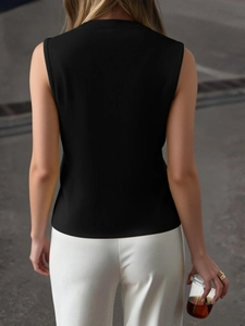 Rear view of a minimalist black sleeveless knit vest styled with white pants outdoors