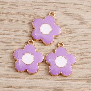 Macro detail of purple daisy alloy charms with gold metallic edges on light wood background