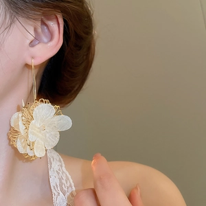 Gros plan de boucles d'oreilles fleur dorées avec pétales blancs sur l'oreille