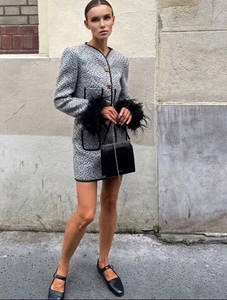 Detail of tweed jacket with gold buttons and feather cuffs paired with a mini skirt