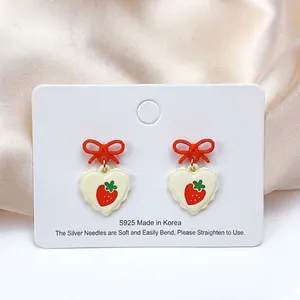 Detail of S925 silver heart strawberry earrings with red bow on champagne silk