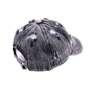Detailed shot of distressed black denim baseball cap featuring vintage frayed holes and metal buckle