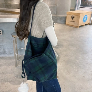 Large green and blue plaid wool tote bag carried by a model in a modern indoor cafe