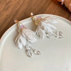 Detail of white fabric floral earrings with shimmering petals and crystal beaded tassels
