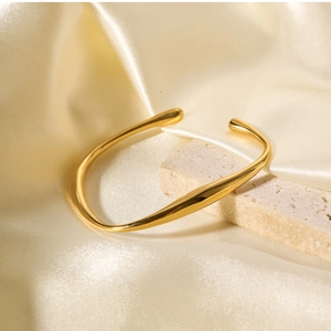 Close-up of golden irregular open bangle on natural stone with cream silk background