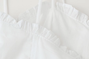 Detail of white spaghetti strap dress with ruffled neckline and delicate fabric texture