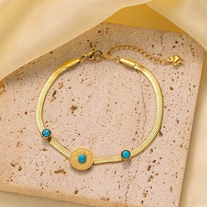 Detalle de pulsera de cadena dorada con piedras verdes y grabado solar sobre piedra