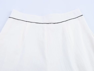 Détail du tissu blanc avec liseré noir à la taille et texture de matière froissée