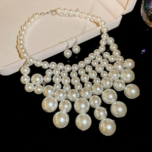 Detailed close-up of multilayer cream white pearl necklace and matching earrings on black background