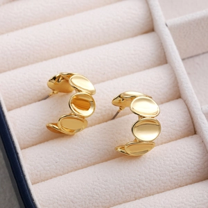 Close-up of golden geometric C-shaped earrings with overlapping discs on velvet display