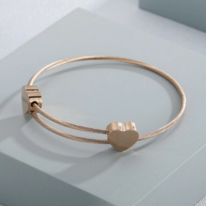 Macro detail of rose gold heart charm on a double-layer twisted wire cuff bracelet