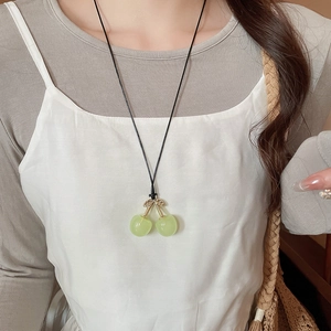 Close-up of translucent green cherry pendant with gold leaves on black wax cord necklace
