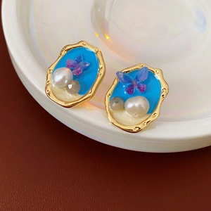 Dettaglio di orecchini vintage in smalto blu con perle e farfalle di cristallo