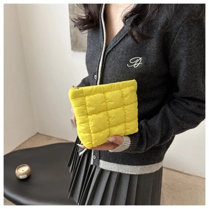 Close-up of a yellow quilted down clutch bag held by a model in a cozy indoor setting