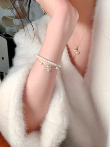 Primer plano de elegante pulsera de perlas camelia y collar dorado en manga de piel blanca