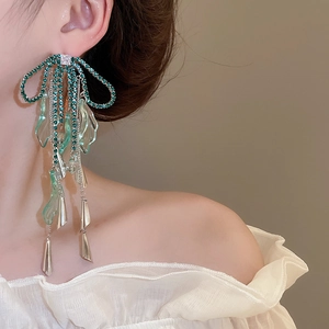 Close-up of sparkling green rhinestone bow earrings with long silver tassels on model