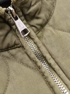 Detailed macro view of the premium metal zipper and olive green twill fabric on the jacket