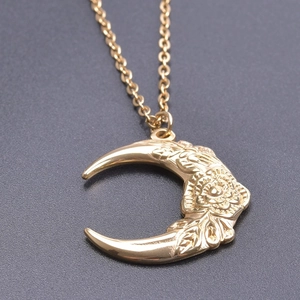 Macro shot of gold crescent moon pendant featuring intricate flower engravings on chain