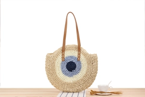 Close-up of circular straw bag with blue contrast weaving and brown leather handles