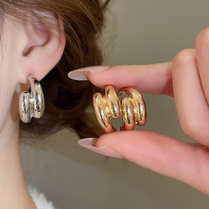Detail of overlapping chunky metallic C-shape hoop earrings in gold and silver finishes