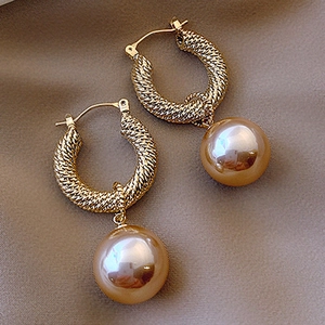 Macro detail of champagne gold woven C-shape hoop earrings with large lustrous pearls