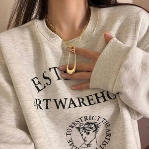 Detail of chunky gold chain necklace featuring a large safety pin pendant on a model