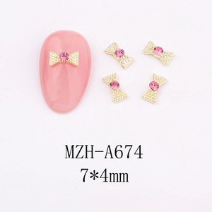 Close-up of golden bow nail art charms with pink rhinestones, size 7x4mm