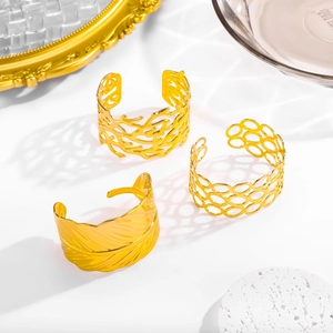 Three gold open bangles with feather and geometric hollow leaf textures on white surface