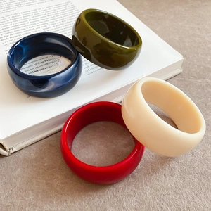 Detail view of wide acrylic bangles in navy, olive, red, and cream on a book