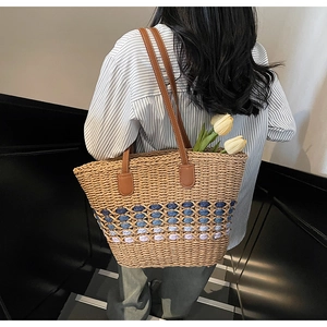 Detail showing the blue gradient woven pattern and brown leather straps on the straw tote bag
