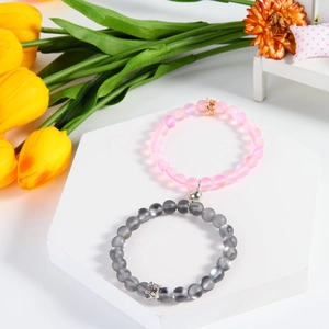 Detail of pink and grey magnetic bracelets with metal crowns on a white stand