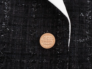Détail des boutons dorés et du passepoil blanc sur un manteau en tweed noir pour femmes