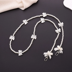 Detail of white pearl strap with bow accents and metal hooks on a dark grey surface