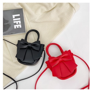 Detail view of small black and red bow cross-body bags on a soft textured fabric
