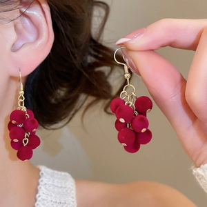 Detailed macro view of red velvet grape-shaped earrings with gold hook on a model