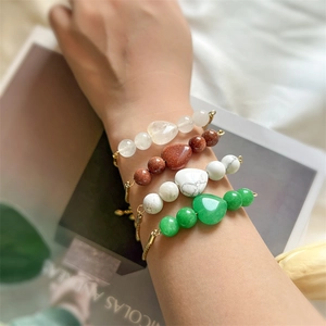 Detailed view of four heart charm beaded bracelets with gold chain on model's wrist