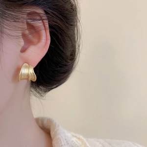 Detail of gold brushed wave stud earrings on model for a minimalist aesthetic