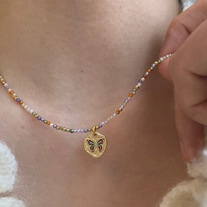 Detail of a colorful beaded necklace with a golden butterfly pendant on a model's neck
