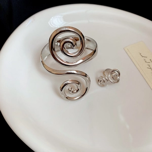 Detail of silver spiral bangle and earrings set on white ceramic tray background