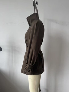 Détail du trench-coat marron foncé avec col montant, ceinture et boucles de manche