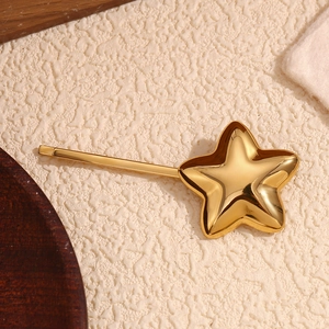 Polished 18K gold-plated stainless steel star hair clip on a beige textured fabric