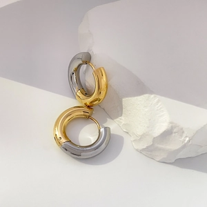 Detail of two-tone gold and silver chunky curved earrings on a white stone background