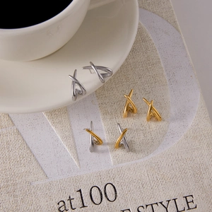 Detailed view of three pairs of X-shaped stainless steel stud earrings in gold and silver