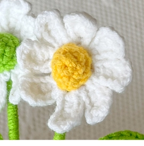Close-up of handmade crochet daisy flower with white petals and textured yellow center