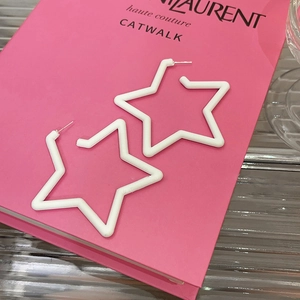 Close-up of oversized white star acrylic earrings placed on a stylish fashion book