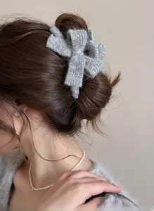 Detail view of a grey knitted bow hair claw clip styled on a brown bun hairstyle