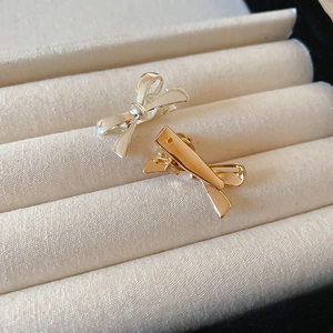Close-up of polished gold and silver bow hair clips with a minimalist metal design